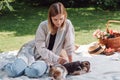 Blonde beautiful girl sitting on white blanket in garden and having picnic at sunny day with cute puppies. Royalty Free Stock Photo