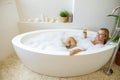 Blonde beautiful young woman lying in bathtub with foam and holding glass of white wine. Royalty Free Stock Photo