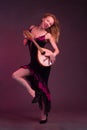 Blonde, in black dress with red flounces, with a mandolin in her hands on a Burgundy background of the Studio Royalty Free Stock Photo