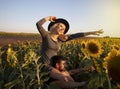 Beautiful young couple kissing in a field of sunflowers at sunset. A blonde in a black hat and a brutal man with a beard.