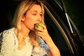 young woman sits in the open trunk of a car and eats a green apple. Royalty Free Stock Photo