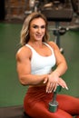Blonde bodybuilder woman is sitting with dumbbell in the gym and posing