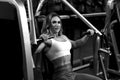 Blonde bodybuilder woman is sitting on training apparatus and posing BW