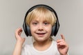 Blonde boy in headphones on light background. Child listens to music and smiles