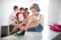 Blonde boy lacing sneakers while classmates gossiping Royalty Free Stock Photo