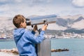 A blonde boy looks through a city telescope against a background of mountains and the sea Royalty Free Stock Photo