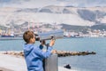 A blonde boy looks through a city telescope against a background of mountains and the sea Royalty Free Stock Photo