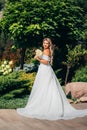 a blonde bride with bouquet Calla Lily in the park in a white long dress.