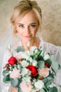 Blonde bride with hair up stands with red bouquet