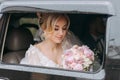 A blonde bride sits in a black car on her wedding day with a bouquet. Royalty Free Stock Photo