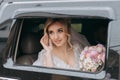 A blonde bride sits in a black car on her wedding day with a bouquet. Royalty Free Stock Photo