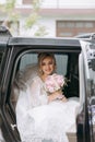 A blonde bride sits in a black car on her wedding day with a bouquet. Royalty Free Stock Photo