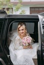 A blonde bride sits in a black car on her wedding day with a bouquet. Royalty Free Stock Photo