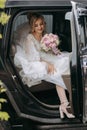 A blonde bride sits in a black car on her wedding day with a bouquet. Royalty Free Stock Photo