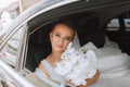 A blonde bride, smiling sincerely, sits in a black car on her wedding day Royalty Free Stock Photo