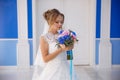 The blonde bride stands on a blue and blue building in a wedding dress and enjoys the aroma of a bouquet of flowers. The Royalty Free Stock Photo