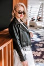 Blonde bride in a white wedding dress, black leather jacket, sunglasses posing for the camera Royalty Free Stock Photo