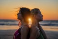 Blonde and brunette girlfriends are clinging back to each other against sunset over the sea. Happy lesbian european couple is Royalty Free Stock Photo