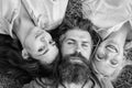 Blonde and brunette lay on his shoulders. Man fall in love both women. Happy threesome. Man bearded hipster lay on grass