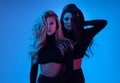 Blonde and brunette models in black clothes looking at camera and posing in studio