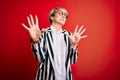 Blonde business woman with short hair wearing glasses and striped jacket over red background afraid and terrified with fear Royalty Free Stock Photo