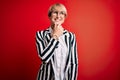 Blonde business woman with short hair wearing glasses and striped jacket over red background with hand on chin thinking about Royalty Free Stock Photo