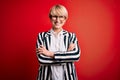 Blonde business woman with short hair wearing glasses and striped jacket over red background happy face smiling with crossed arms Royalty Free Stock Photo