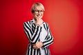 Blonde business woman with short hair wearing glasses and striped jacket over red background looking confident at the camera Royalty Free Stock Photo