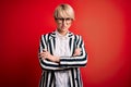 Blonde business woman with short hair wearing glasses and striped jacket over red background skeptic and nervous, disapproving Royalty Free Stock Photo