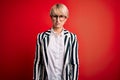 Blonde business woman with short hair wearing glasses and striped jacket over red background skeptic and nervous, frowning upset Royalty Free Stock Photo