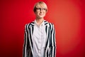 Blonde business woman with short hair wearing glasses and striped jacket over red background smiling looking to the side and Royalty Free Stock Photo