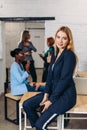 Blonde business woman smiles at camera with colleagues working in background Royalty Free Stock Photo