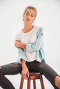 Blonde casual woman sits on stool and looks to side