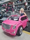 Blonde Caucasian girl sitting posing in large huge pink Cadillac car in kids children store Toys Are Us. Royalty Free Stock Photo