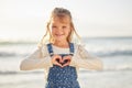 Blonde caucasian little girl enjoying a day at the beach, making a heart shape gesture with her hands. Small child Royalty Free Stock Photo