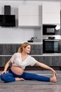 blonde caucasian mom-to-be, pregnant female in sportive clothes doing exercises on fitness mat