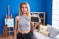 Blonde caucasian woman holding blackboard with new home text thinking attitude and sober expression looking self confident