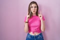 Blonde caucasian woman standing over pink background pointing up looking sad and upset, indicating direction with fingers, unhappy Royalty Free Stock Photo