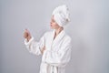 Blonde caucasian woman wearing bathrobe looking proud, smiling doing thumbs up gesture to the side