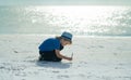 Blonde child in a hat and shirt draw pictures in the sand by the sea. Travel and recreation with children. Childrens