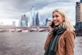 A blonde city woman talking on her cellphone in front of the urban skyline of London, Royalty Free Stock Photo