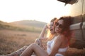 Blonde and curly-haired smiling ladies sitting next to the car