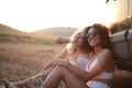 Blonde and curly-haired smiling ladies sitting next to the car