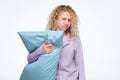 Blonde curly woman holding blue pillow feeling sleepy Royalty Free Stock Photo