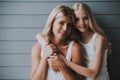 Blonde cute girl hugs blonde mother on wooden background. Royalty Free Stock Photo