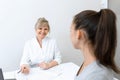 Blonde doctor woman in a white coat sitting at a table in a medical office and conversation to a patient Royalty Free Stock Photo