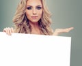 Blonde fashion model girl holding white empty paper board background. Beautiful blonde woman Royalty Free Stock Photo