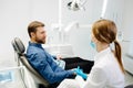 Blonde female dentist in dental office talking with male patient and preparing for treatment. Handsome bearded man in dentist Royalty Free Stock Photo