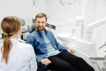 Blonde female dentist in dental office talking with male patient and preparing for treatment. Handsome bearded man in dentist Royalty Free Stock Photo