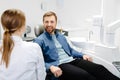 Blonde female dentist in dental office talking with male patient and preparing for treatment. Handsome bearded man in dentist Royalty Free Stock Photo